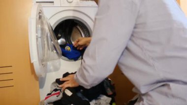 Çamaşır makinesinde çocukların çamaşırlarını yıkayan bir adam. Cinsiyet ve ev işleri, eşitlik kavramlarını bir kenara bırak ve bir adamın evde ailesine ve karısına yardım et..