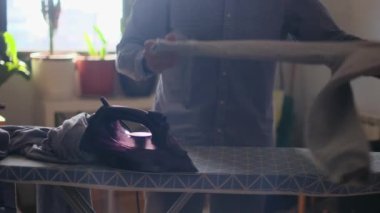 Çocuk kıyafetlerini yemek odasında ütüleyen bir adam. Cinsiyet ve aile görevleri, eşitlik kavramlarını bir kenara bırak ve adamın ailesine ve karısına evde yardım et.