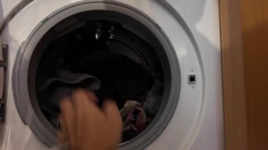 Çamaşır makinesine çamaşır koyan adam.