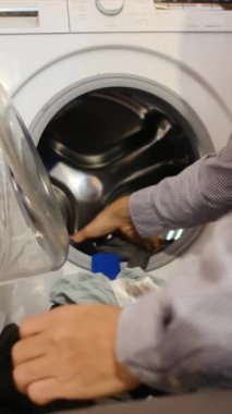 Adam otomatik çamaşır makinesinden giysileri çıkarıyor..