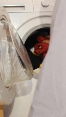 Çamaşır makinesine çamaşır koyan adam.