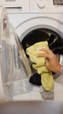 Çamaşır makinesine çamaşır koyan adam.