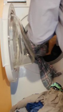 Adam otomatik çamaşır makinesinden giysileri çıkarıyor..