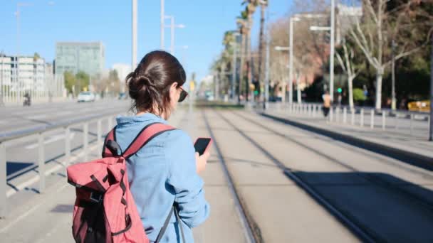 Νεαρή Γυναίκα Που Χρησιμοποιεί Smartphone Λευκό Περιμένει Τραμ Στο Σταθμό — Αρχείο Βίντεο