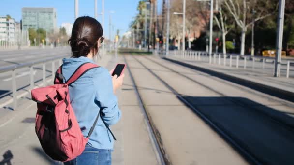 Giovane Donna Utilizzando Smartphone Bianco Attesa Tram Stazione Durante Giorno — Video Stock