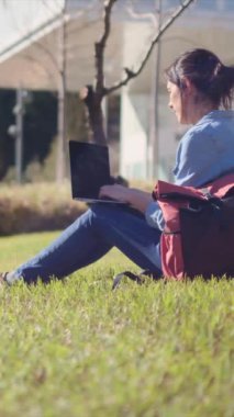 Kampüste laptopuyla ders çalışmaya dalmış bir üniversite öğrencisi, açık hava sükunetini kucaklıyor, e-öğrenme yolculuğuna güveniyor..