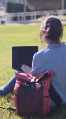 Kampüste laptopuyla ders çalışmaya dalmış bir üniversite öğrencisi, açık hava sükunetini kucaklıyor, e-öğrenme yolculuğuna güveniyor..