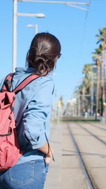 Sırt çantalı genç bir kadın tramvayda ya da şehir tren peronunda binmeye hazır bekliyor. Spor kıyafetleri, seyahat, rutin, keşif ve çevre dostu ulaşımı somutlaştırıyor..