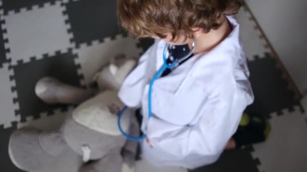 小男孩穿着医用长袍和听诊器玩玩具大象 — 图库视频影像