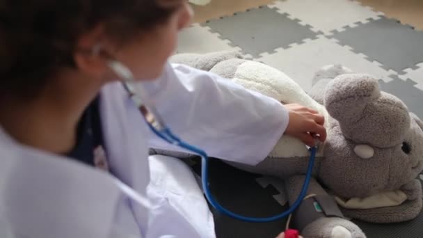 Mały Chłopiec Noszący Szlafrok Medyczny Stetoskopem Bawiący Się Zabawkowym Słoniem — Wideo stockowe