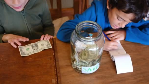 Маленькие Мальчики Собирают Долларовые Банкноты Банку Экономии Сидя Деревянным Столом — стоковое видео