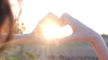 Bulanık tarımsal ortamda, kadın ellerinde kalp şeklinde parlayan güneş.