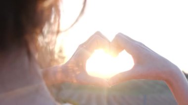 Bulanık tarımsal ortamda, kadın ellerinde kalp şeklinde parlayan güneş.