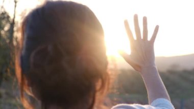 Bulanık tarım arazisinde avuçlarını güneşe uzatan kadın.