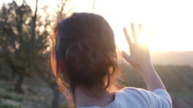 Bulanık tarım arazisinde avuçlarını güneşe uzatan kadın.