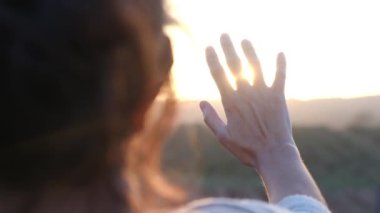 Bulanık tarım arazisinde avuçlarını güneşe uzatan kadın.