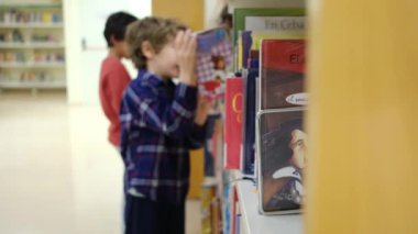 Küçük çocuklar kütüphanede kitap seçiyor.