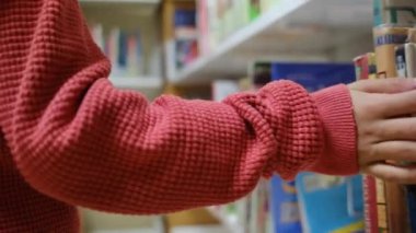 Küçük çocuk kütüphanede kitap seçiyor.