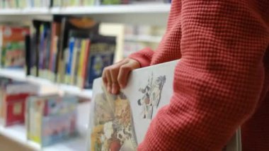 Kitaplı küçük çocuk kütüphanede yürüyor.