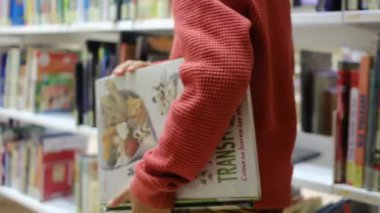 Kitaplı küçük çocuk kütüphanede yürüyor.