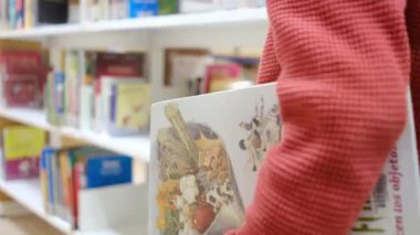 Kitaplı küçük çocuk kütüphanede yürüyor.