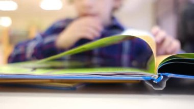 Bulanık küçük çocuk masada kitap okuyor.