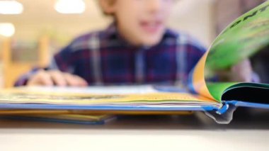 Bulanık küçük çocuk masada kitap okuyor.