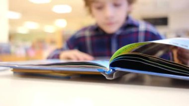 Bulanık küçük çocuk masada kitap okuyor.