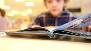 Bulanık küçük çocuk masada kitap okuyor.