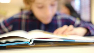 Bulanık küçük çocuk masada kitap okuyor.