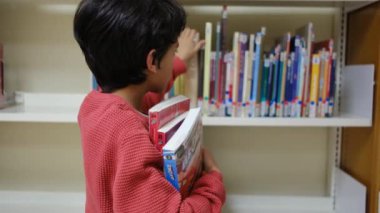 Küçük çocuk kütüphanede kitap seçiyor.
