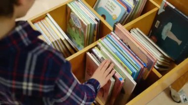 Küçük çocuk kütüphanede kitap seçiyor.