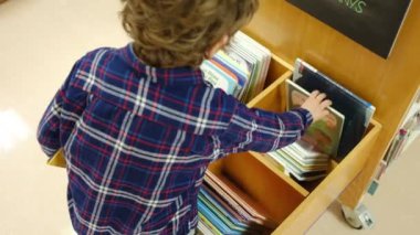 Küçük çocuk kütüphanede kitap seçiyor.