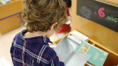 Küçük çocuk kütüphanede kitap seçiyor.