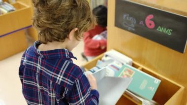 Küçük çocuk kütüphanede kitap seçiyor.