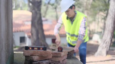 Üniforma giyen ve miğfer takan bulanık kadın işçilerin ön planında denge düzeyi cetveli güneşli bir günde inşaat alanında kaseye çimento karıştırıyor.