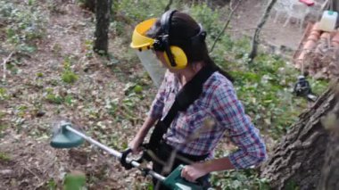 Kadın bahçıvan parkta ya da ormanda çim biçme makinesiyle bitki kesiyor. 