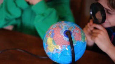 Küçük çocuklar masadaki Dünya gezegenini inceliyor.