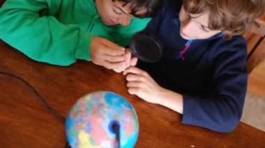 Küçük çocuklar masadaki Dünya gezegenini inceliyor.