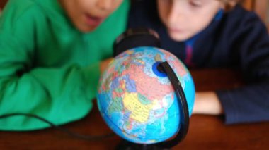 Küçük çocuklar masadaki Dünya gezegenini inceliyor.