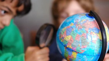 Küçük çocuklar masadaki Dünya gezegenini inceliyor.