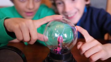 Küçük çocuklar masada yıldırımla plazma topu çalışıyor.