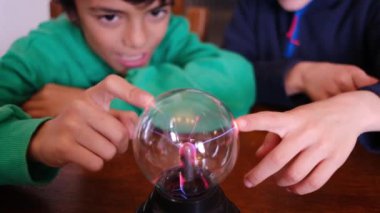 Küçük çocuklar masada yıldırımla plazma topu çalışıyor.