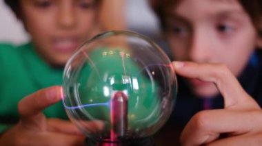 Küçük çocuklar masada yıldırımla plazma topu çalışıyor.