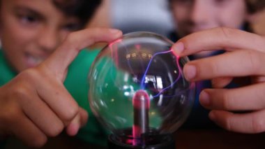 Küçük çocuklar masada yıldırımla plazma topu çalışıyor.