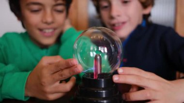 Küçük çocuklar masada yıldırımla plazma topu çalışıyor.