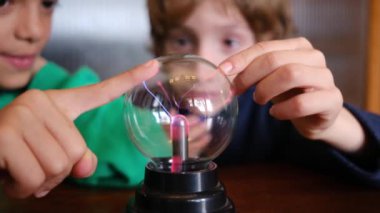 Küçük çocuklar masada yıldırımla plazma topu çalışıyor.