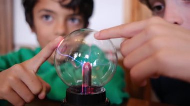 Küçük çocuklar masada yıldırımla plazma topu çalışıyor.