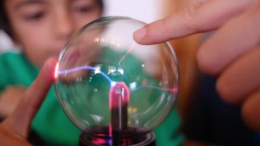 Küçük çocuklar masada yıldırımla plazma topu çalışıyor.