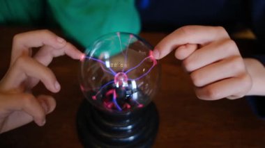 Küçük çocuklar masada yıldırımla plazma topu çalışıyor.
